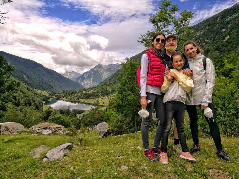 Família de pare i filles envoltats de la natura del Parc Nacional d'Aigüestortes i l'estany Llebreta al fons.